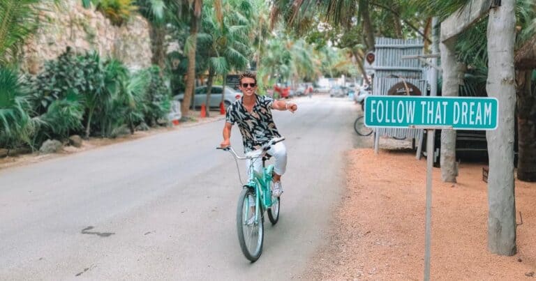 man doing Tulum bike tours pointing to follow that dream sign