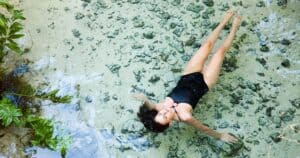 woman in black swimsuit swimming in gran cenote tulum mexico