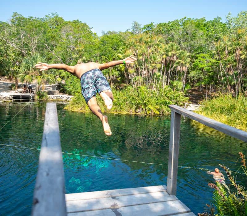 man jumping off diving platform at tulum cenote cristal